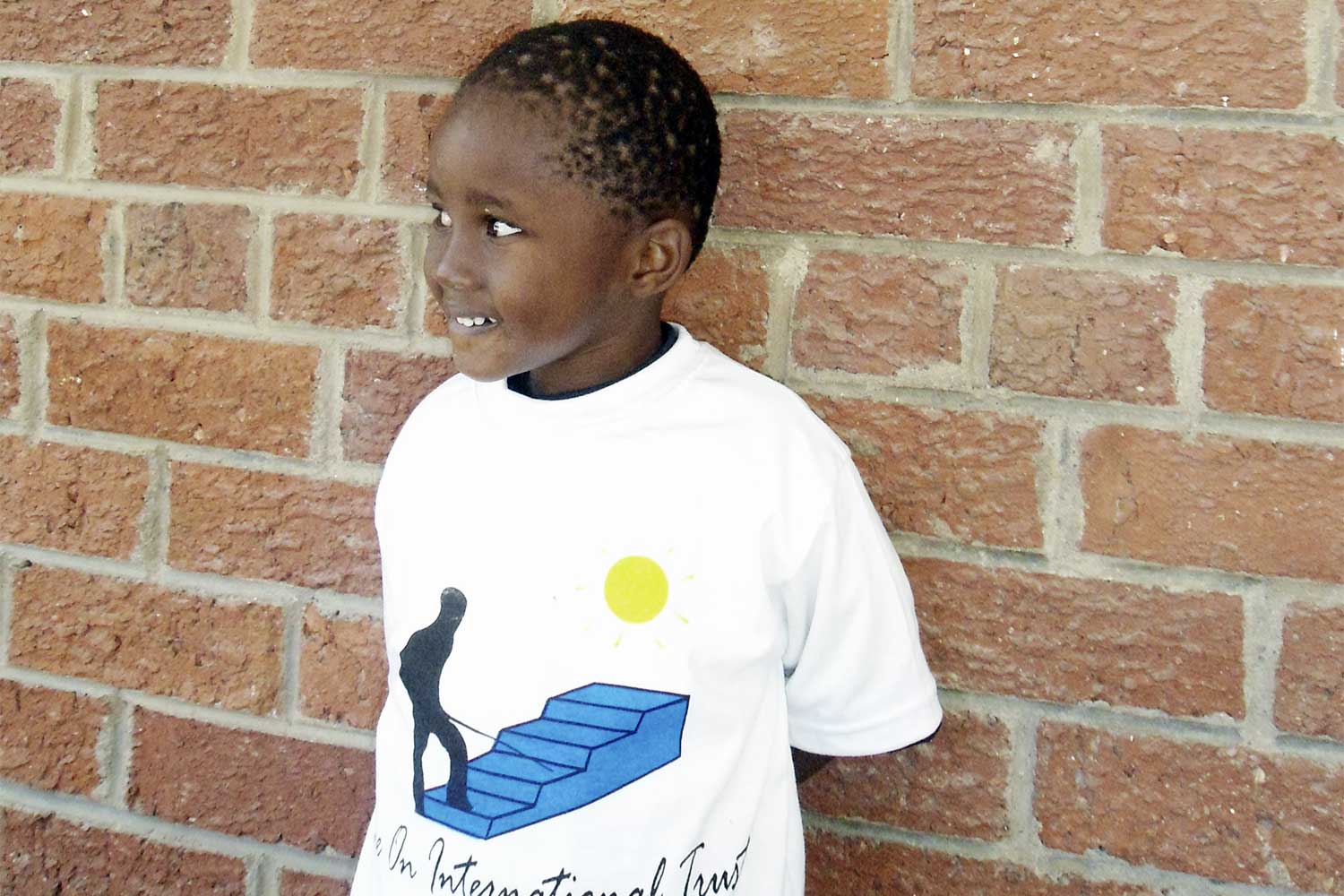 Boy in front of a wall with Shine on International Trust shirt